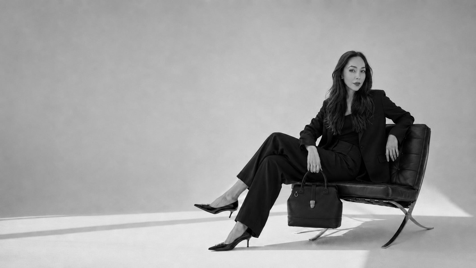 Angelina Walker the Founder of TAH Handbags sitting on a chair with a Leather Doctor bag in hand, in black and white 
