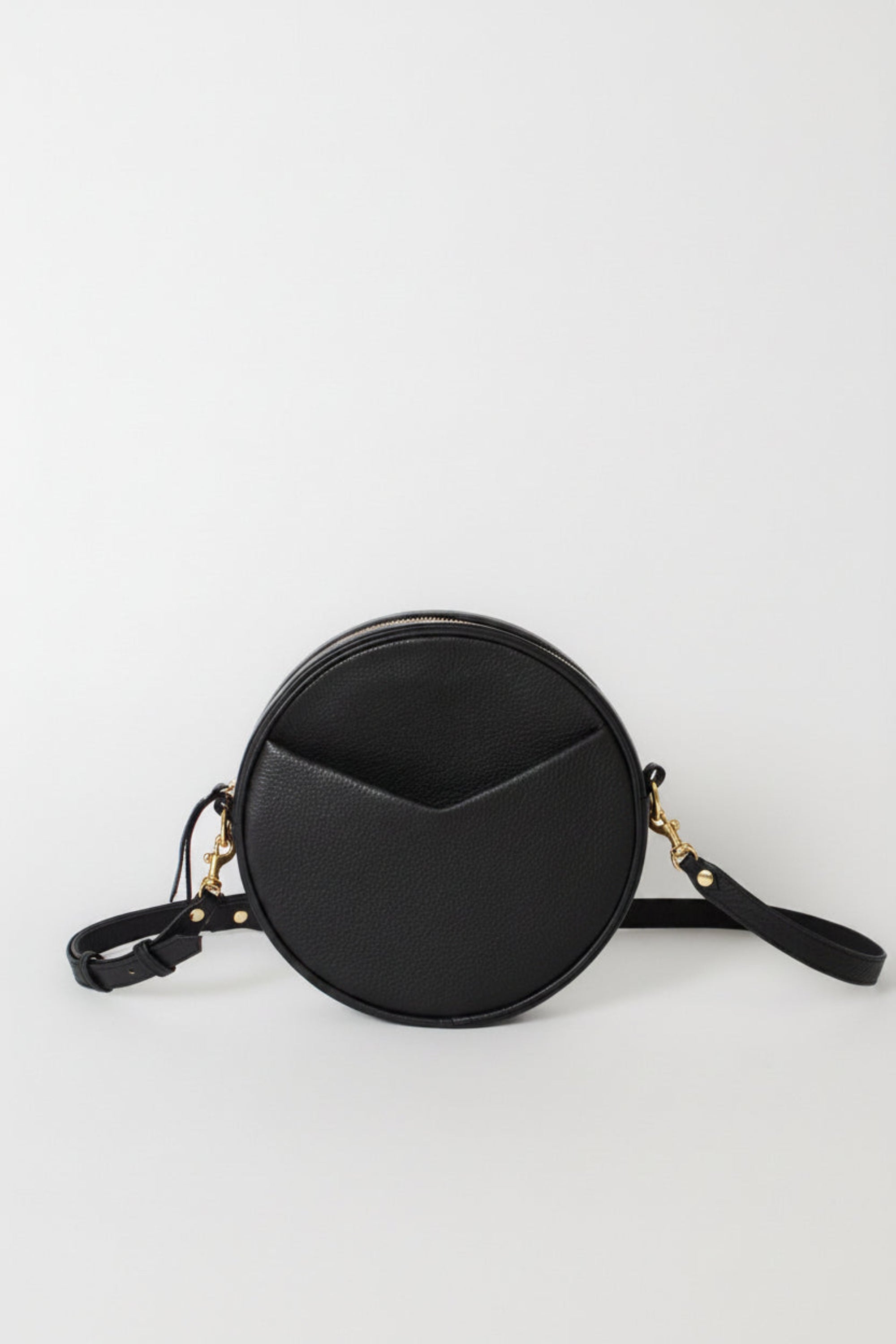 A black round crossbody bag with a crescent-shaped front pocket and a black shoulder strap, accented with gold-tone hardware.