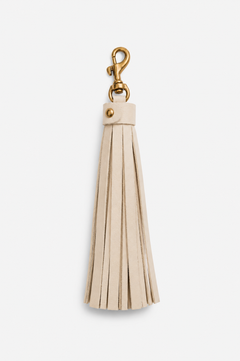 An ivory leather tassel keychain with a gold-tone metal lobster clasp and rivet, shown against a plain light gray background.