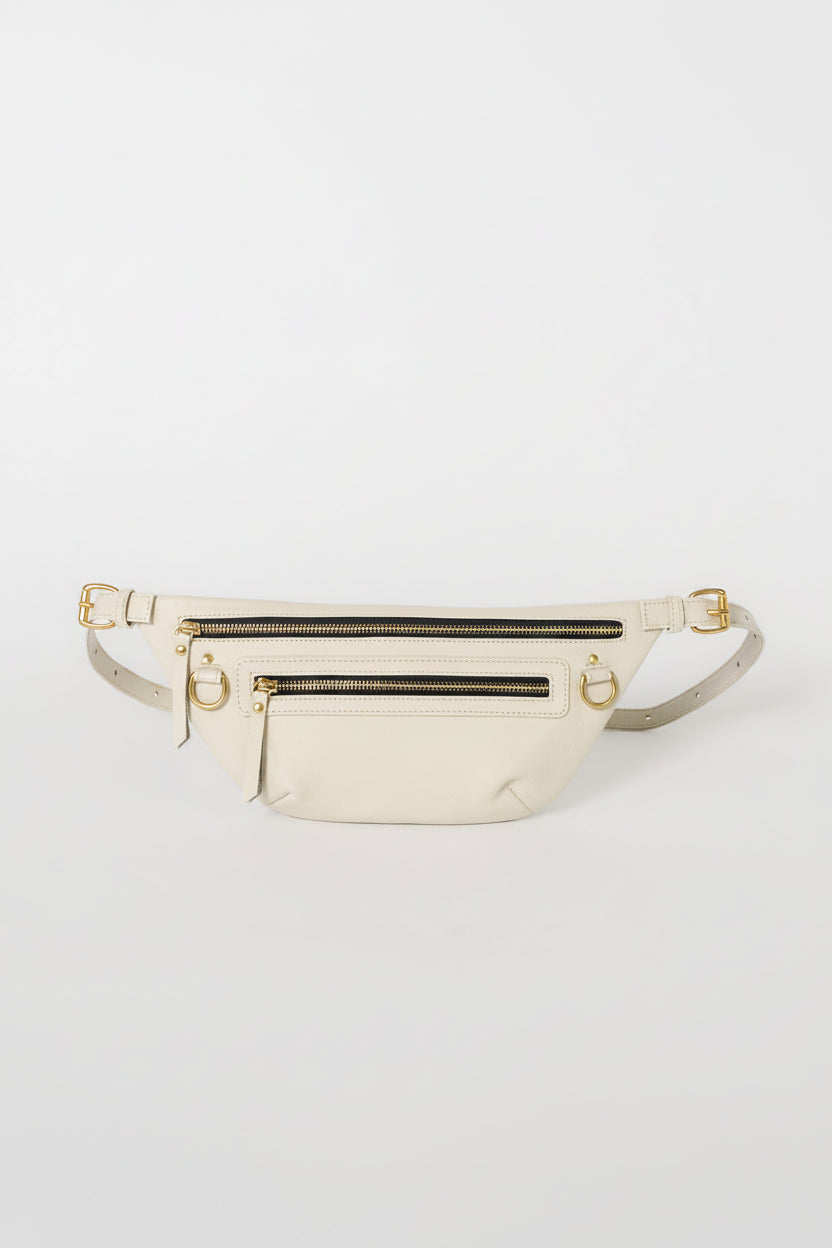 Nomad Fanny Pack in bone leather, front view with adjustable strap laid flat, featuring gold hardware, two zip compartments, D-rings, and a front pocket — a hands-free belt bag for travel and everyday wear