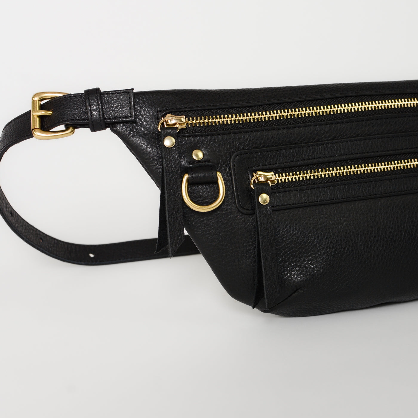 Black leather fanny pack belt bag detail featuring gold hardware, adjustable strap, and multiple zip pockets, highlighting functional design and everyday durability.