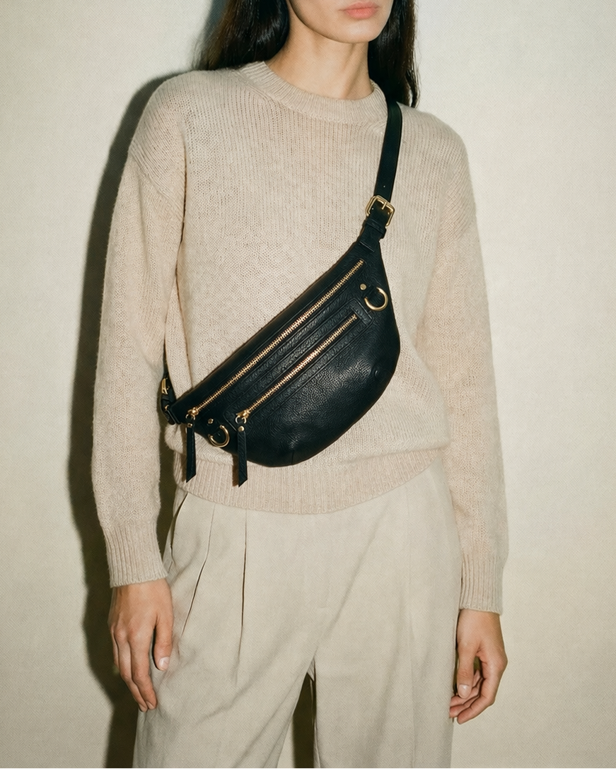 Black leather fanny pack belt bag worn crossbody, featuring an adjustable strap, multiple zip pockets, and gold hardware, designed as a refined, hands-free everyday bag for travel, errands, and daily essentials.