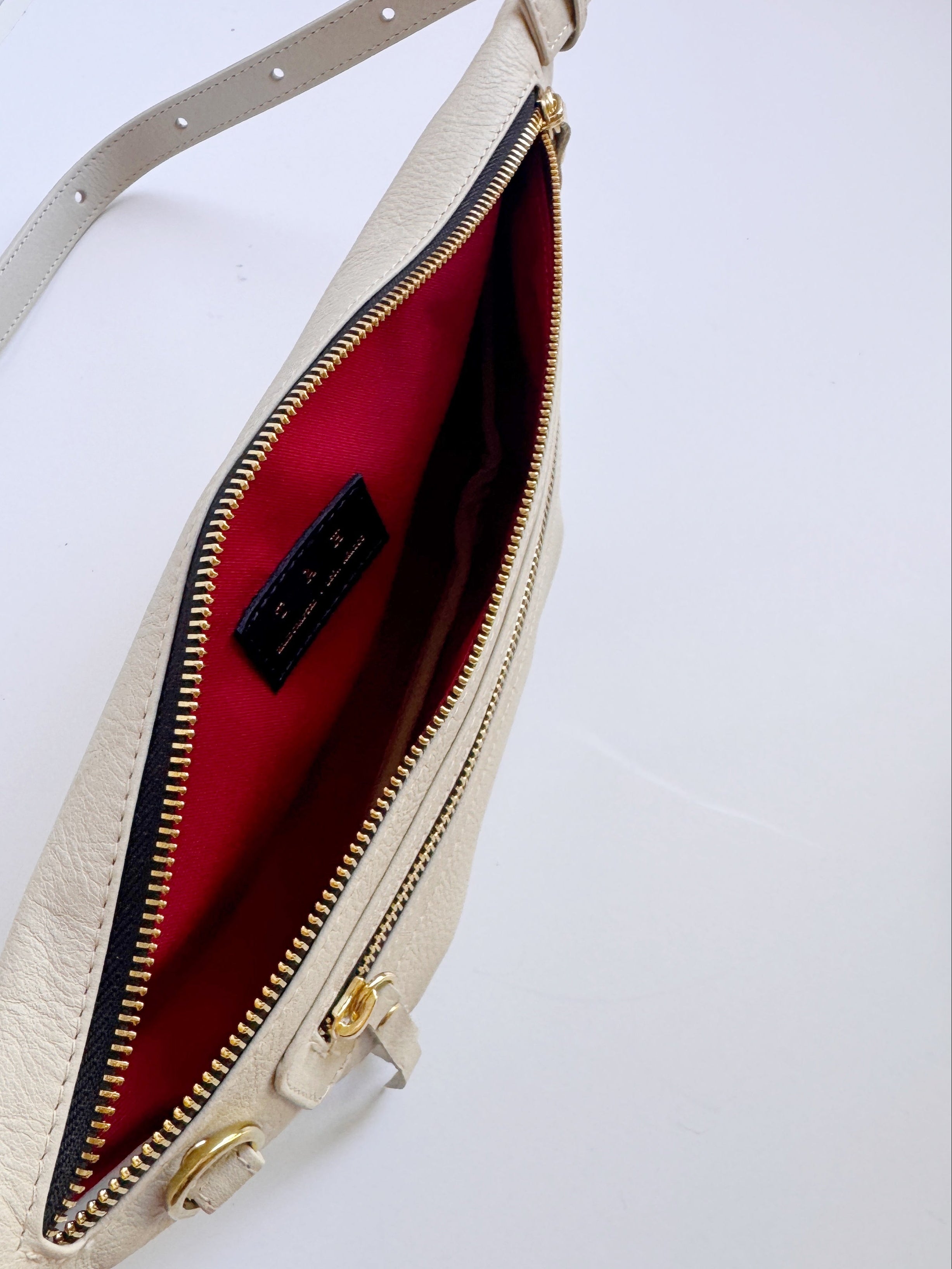 Off white leather sling bag  designed for travel and hands-free. Can also be worn as a fanny pack. This image shows the red interior of one of the front pockets. 