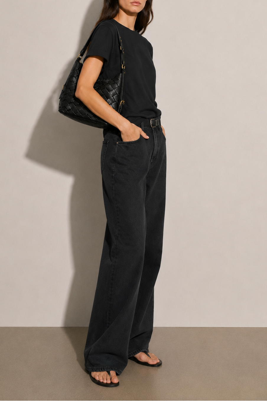 A handwoven leather bag in the color black with gold buckles and hardware worn with an all-black outfit