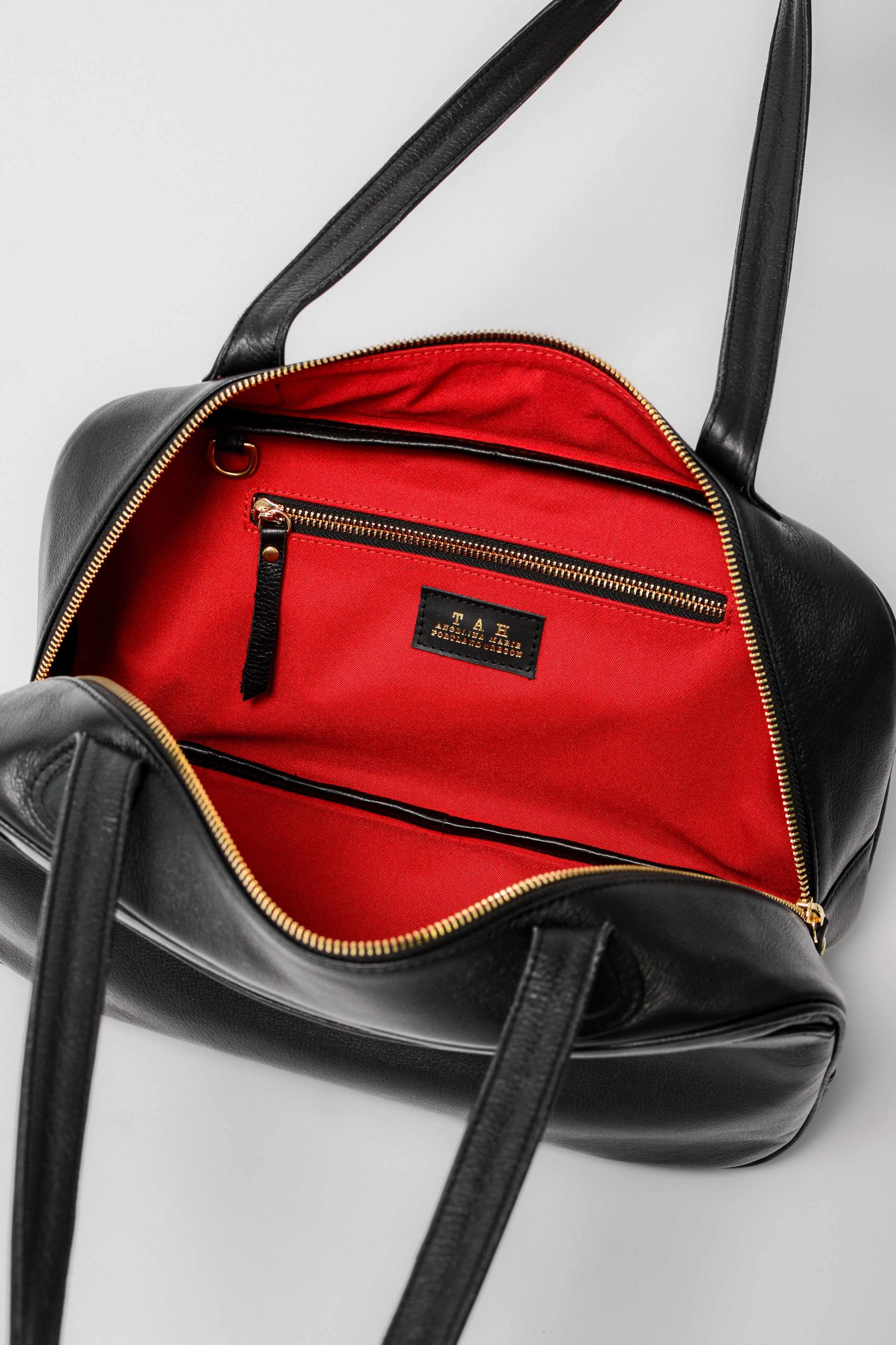 Interior of the Ari Bowler Bag in black leather featuring a red lining, zip pocket, and organized compartments for everyday essentials.