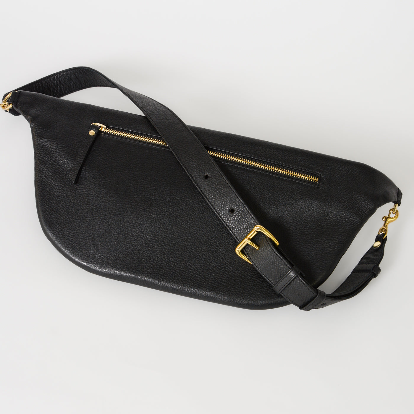 Black leather commuter sling bag shown from back angled view, featuring adjustable strap, zip pocket, and gold hardware, designed for secure, hands-free everyday use.