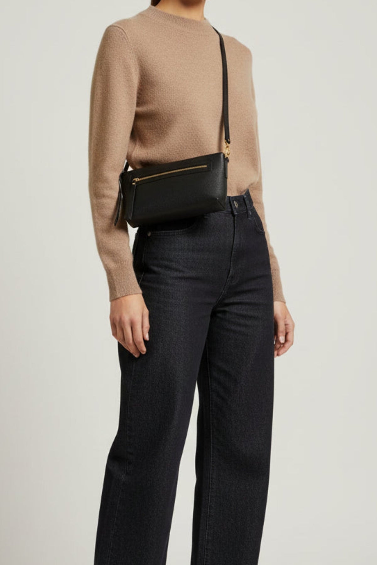 Black leather Ella shoulder bag worn crossbody on model from side view, featuring a structured silhouette, front zip pocket, and gold hardware for a streamlined everyday look.
