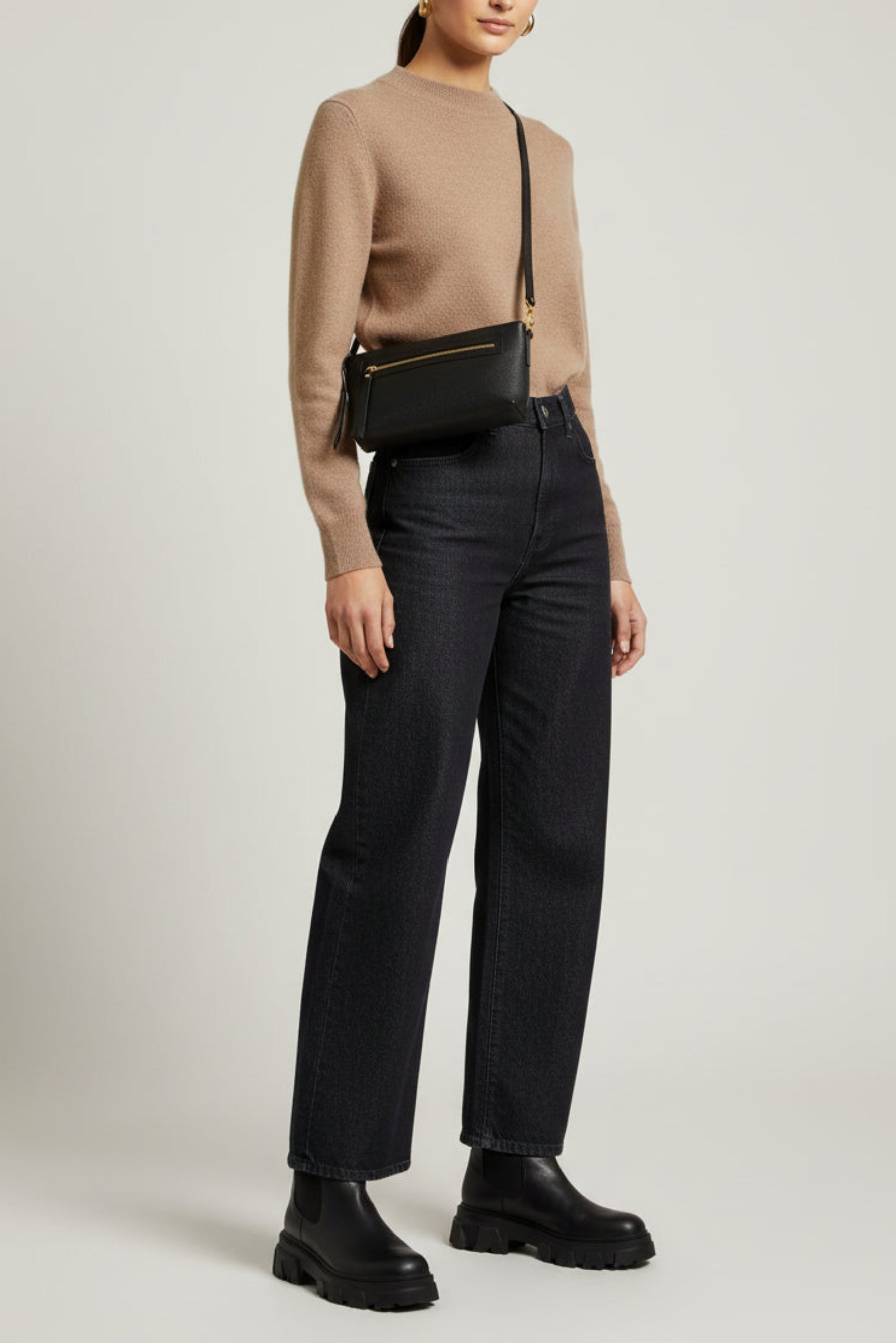 Black leather Ella shoulder bag worn crossbody on model from side view, featuring a structured silhouette, front zip pocket, and gold hardware for a streamlined everyday look.
