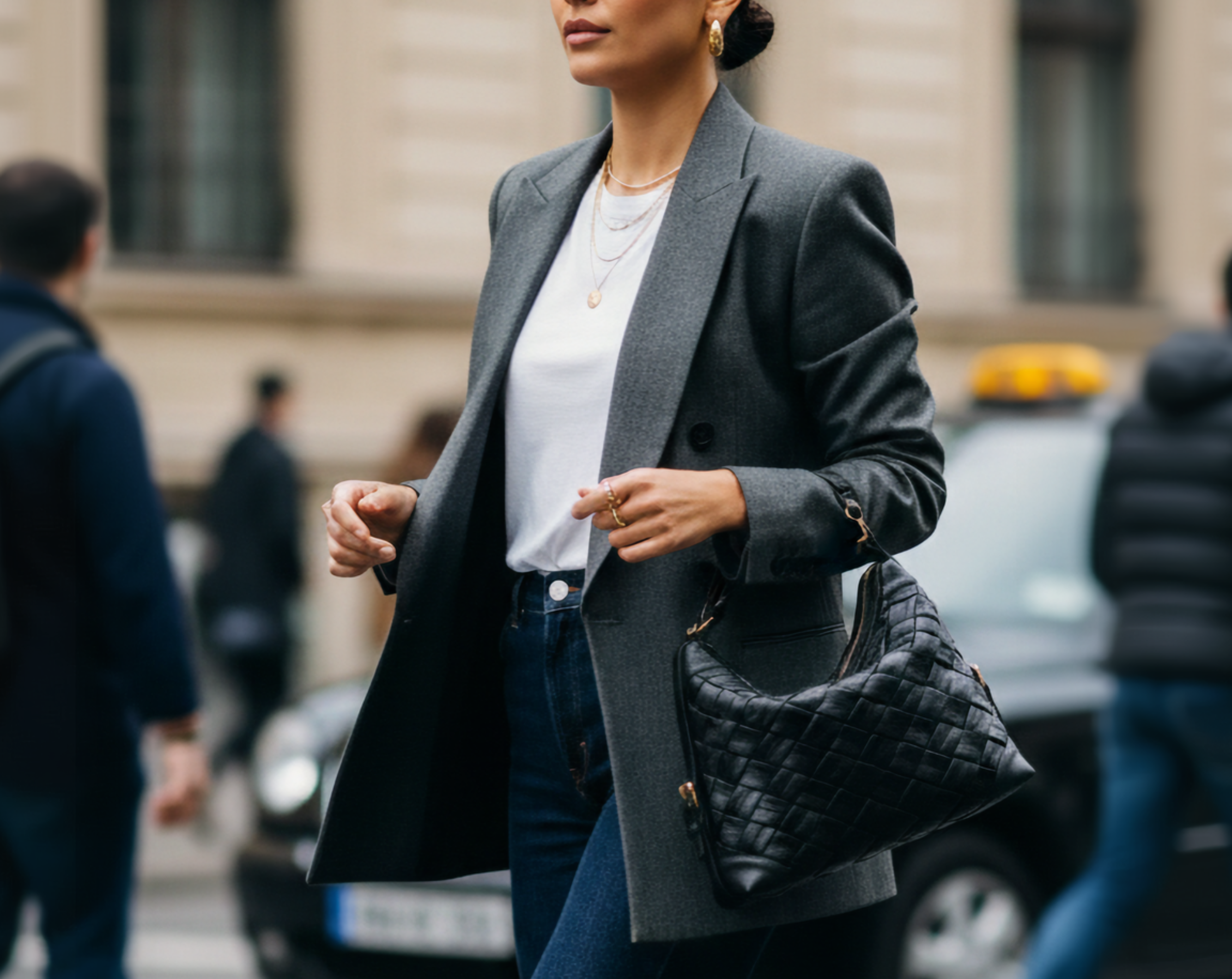 Close-up lifestyle image of a model carrying the black Selena Handwoven leather bag, featuring intricate woven detailing, styled with a blazer in an urban setting.